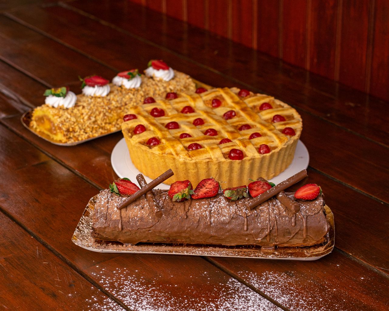 A tempting display of pastries including chocolate roulade, fruit tart, and nut cake on a wooden table.